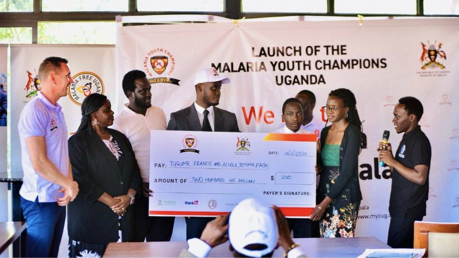 Guests and youth champions present a 200 US dollar award cheque to Tugume Francis and Achola Jemimah Faith at the launch of Malaria Youth Champions Uganda