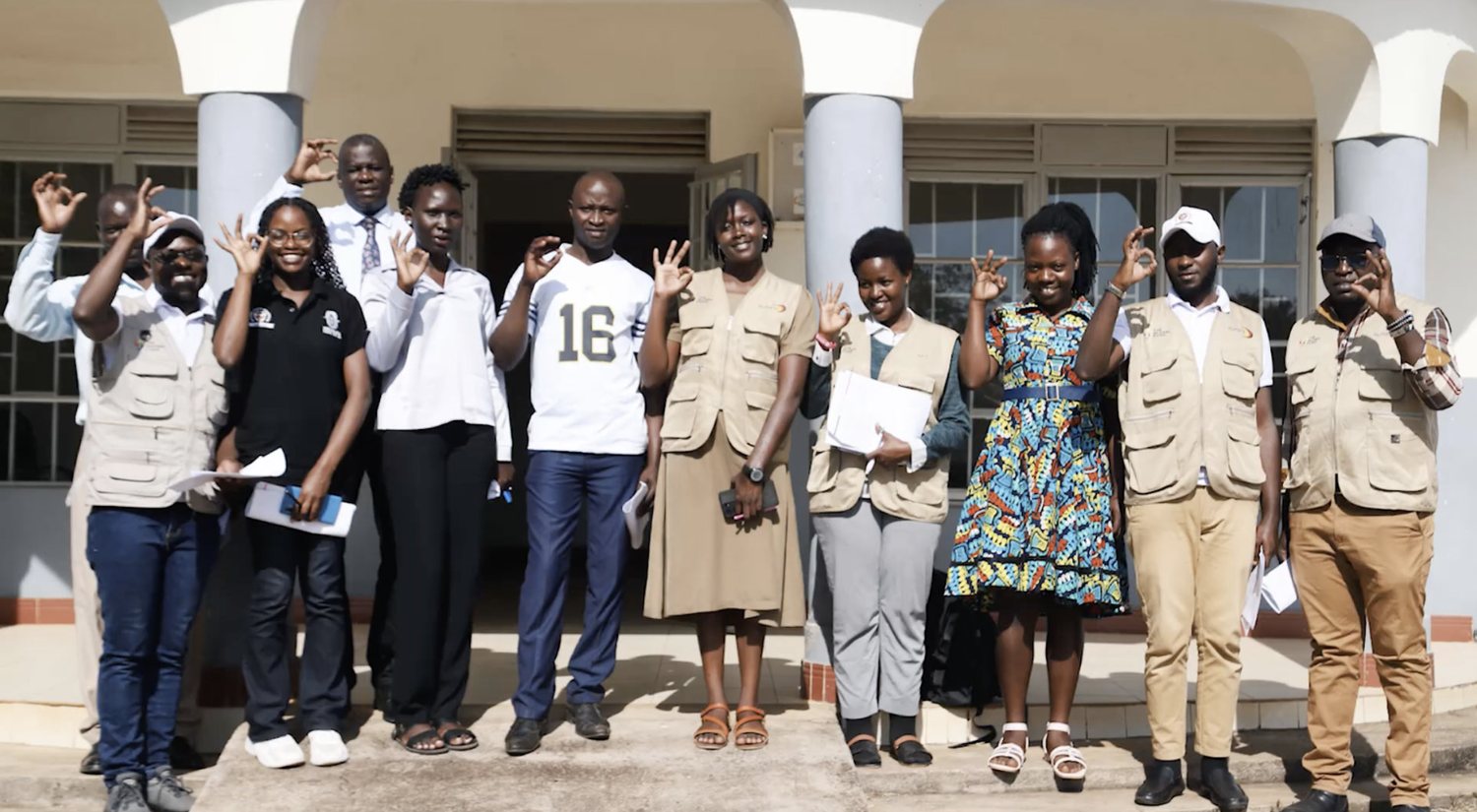 The MYCU team and Bukedea district health partners outside Nalugai Health Centre III, making the OK hand sign together