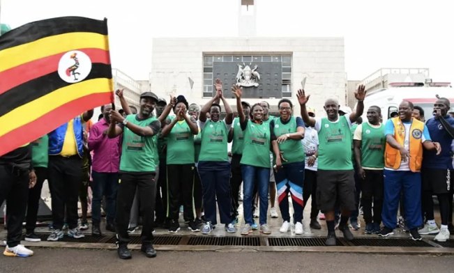 Members of Parliament and malaria champions in green T-shirts cheer outside Uganda's Parliament building, one waving the Uganda flag