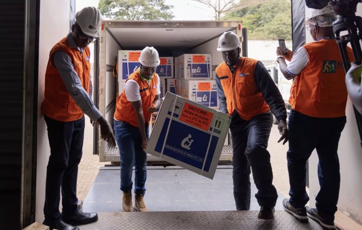 Workers in hard hats and orange vests unload a box of malaria vaccines from a refrigerated truck