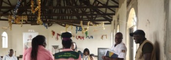 A facility in-charge addresses community members and youth champions in a hall
