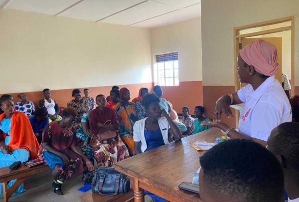 A champion in a white MYCUG shirt leads a community meeting on using bed nets