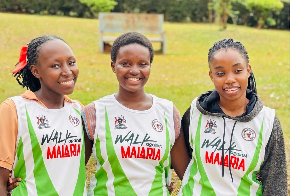 Three young women in Walk Against Malaria vests smiling together on a lawn